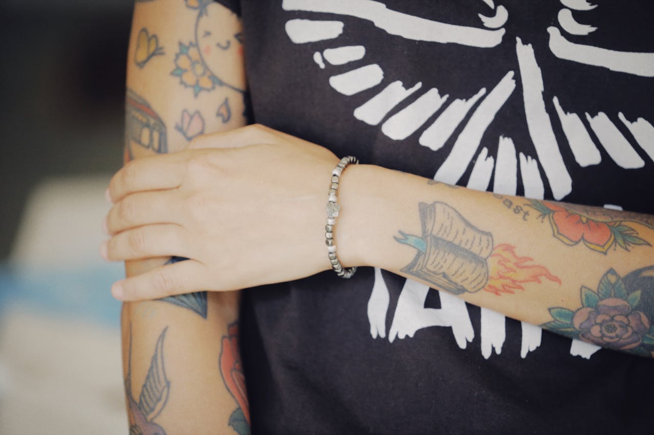 A close-up of a tattooed arm wearing a stylish bracelet, showcasing intricate tattoo designs.